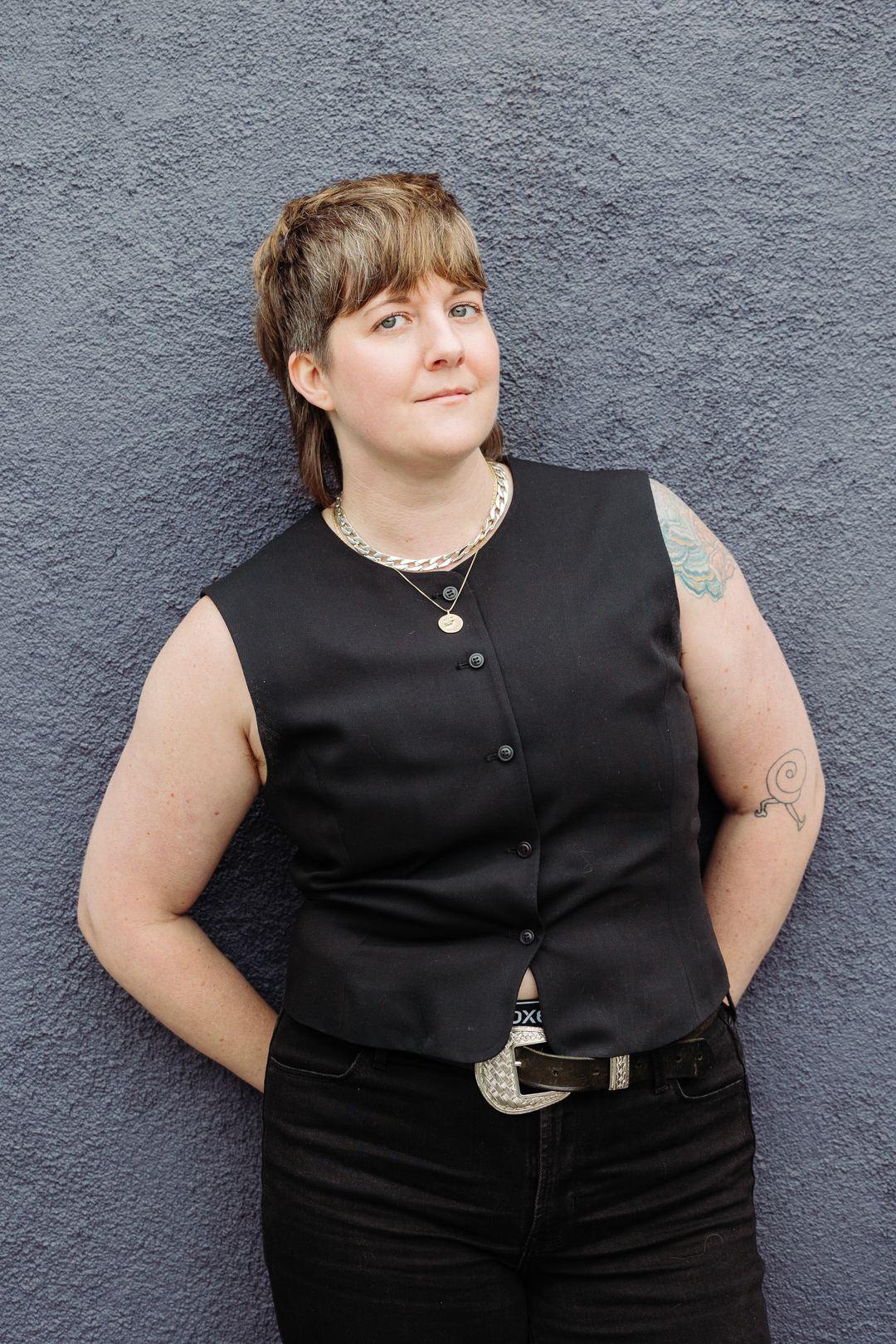person looking toward camera posed standing against a blue wall